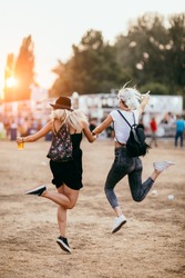 Two female friends jumping and having fun at music festival. Back view