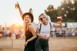 Two female friends drinking beer and having fun at music festival