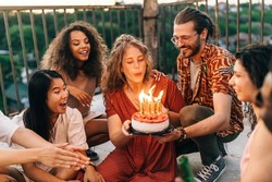 A birthday girl blows candles and wishes a wish while her friends look at her. A man holds a birthday cake while a girl blows the candles. The rest of the crew smiles and looks at her.