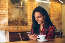 Young african woman at cafe drinking coffee and using mobile phone
