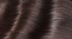 A closeup view of a bunch of shiny straight brown hair in a wavy curved style.