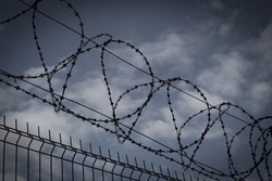 Barbed wire fence in dark colors on background with dark sky. Metaphor concept of prison, jail, arrest. Prohibbited zone and area