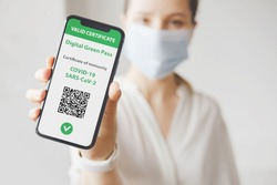 Young caucasian woman in mask holding smartphone with digital green pass and QR code on the screen. Health passport or certificate of immunity. Traveling without restrictions. Vaccinated person