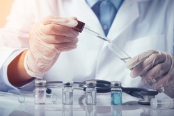 Doctors are dropping chemicals into a test tube to test an antiviral vaccine in the laboratory. Containing vials, vaccines, test tubes, syringes on a white table