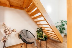 A cozy reading corner at home with a small armchair in modern design, accompanied by a similar size coffee table. It is simply located under wooden stairs and is complemented by home-grown vegetation.