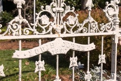 Close-up details of vintage metalwork, a white wrought iron fence with filigree and flowers dated 1890, still elegant but thick with layers of paint, lichen, and rust.