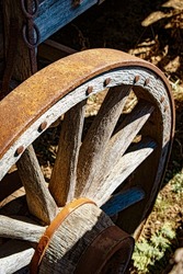 Old wagon wheel in sunlight and shadow. Rusty iron and weathered wood. Close-up with selective focus.