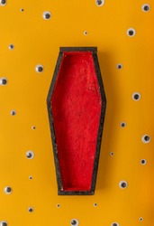 Halloween yellow background with an open red-black coffin in the center, around a scattering of plastic eyes of different sizes.  