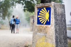 the yellow scallop shell signing the way to santiago de compostela on the st james pilgrimage route with two pilgrims chatting on the background