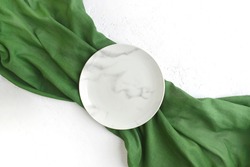 Empty marble plate with green fabric on white textured background. Minimalist summer table setting. Eco friendly style. Top view. 