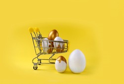 Mock up Easter composition with shopping trolley and  golden decorated eggs on yellow background. Minimalist concept for holiday or sale. Banner. Copyspace. 