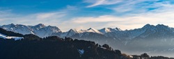 Panorama view of the snowy mountains between Switzerland, Liechtenstein and Austria. in foreground Austrian Alp with meadows and huts in the middle of the woods and in Background mountain range peaks
