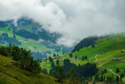 Adelboden panorama with alpine farmhouses and trees, forests and green meadows on a cloudy day. valley with holiday destination village in Swiss alps. interesting scenery with alpine weather mood
