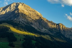 the morning sun illuminate the clouds and the peaks of Swiss mountains around Adelboden. first light in the valley from Boden, under the high mountain big wager, with green meadows, forests and rocks