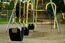 Swing set at a playground that is empty. Lighting is warm due to the being taken at sunset