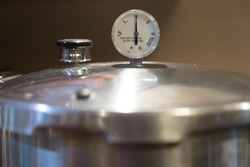 A stainless steel pressure cooker lid with pressure gauge reading 10 pounds of pressure. Pressure canners are used to can vegetables from the garden.