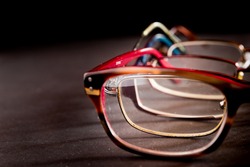 Multiple pairs of eyeglasses on a black surface. Only one half of the glasses are visible. The glasses are nested within each other and are visible through the lens of each pair.