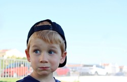 A blond boy in a black cap looks away in wonder. A five-year-old boy with a sly look. 