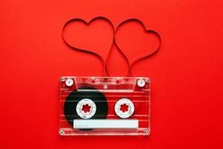 Vintage audio cassette with loose tape shaping two hearts on red background 