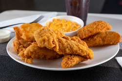A view of a plate of breaded chicken tenders, with potato wedges and macaroni and cheese sides.