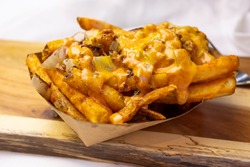 A view of a basket of loaded fries, on a wooden cutting board, in a restaurant or kitchen setting.