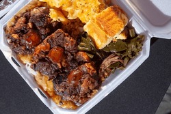 A top down view of an entree of smothered oxtails, with a side of mac n cheese, corn bread, and collard greens.