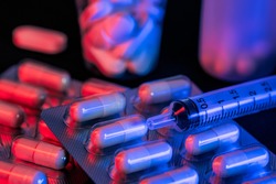Capsule and pills medicines with syringe with black background and red and blue lights