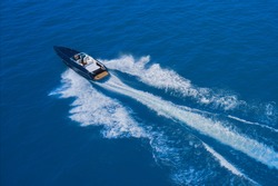 High-speed yacht of blue color fast motion on blue water in the rays of the sun top view.  Speed boat movement at high speed aerial view. Top back view of the boat.