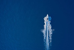 Top view of a white boat sailing to the blue sea. Large speed boat moving at high speed. Travel - image. Drone view of a boat sailing. Motor boat in the sea.