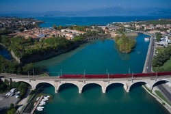 Red train blur in motion on a bridge over a river in Italy. Red high-speed train in motion on the bridge over the river aerial view. The high-speed train is moving fast across the bridge.