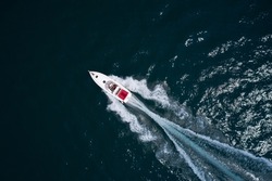 Drone view of a moving white boat on the water. People rest on a boat. Speedboat moves fast on the water top view. Speed boat with red seats aerial view.