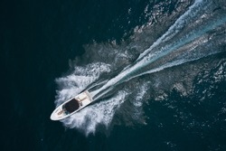 Speedboat on dark water aerial view. Boat trip at sea. White boat with a black awning movement on the water drone view.