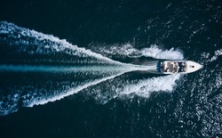 Big boat in motion on the water top view. Luxury yacht with people moving fast on dark blue water making a white trail behind the boat, aerial view.
