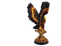 Figurine, statuette an eagle, hawk, peregrine, falcon, kite sitting on stand on white background. Wild bird sculpture with open wings inlaid with natural Honey amber stones. Use for interior design.