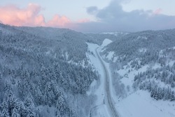 The highway passes through the pass in winter, top view of the snowy forest in winter. Snow-covered road runs through the forest in the mountains through the pass in December.