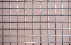 Metal chrome grate with a square mesh on a pink background.