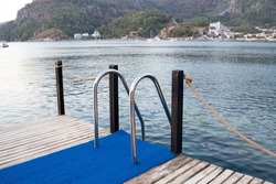 Metal handrails and ladder to descend into the water on a wooden pier of a sea bay - a place for swimming. Wooden pier with ladder for comfortable entrance in the sea.