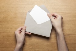 A female(woman) hand hold(open) a envelope and post card on the wood desk, top view at the studio. 