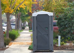 Port a potty sitting in a driveway next to the sidewalk in a neighborhood tree lined and picturesque. Facilities for construction crew in an affluent neighborhood.