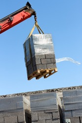 unloading of construction material on the construction site using a hydraulic lifting crane. a pallet with a expanded clay block on the background of a blue sky. lifting crane boom