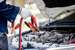 Close up of automotive mechanics holding jump leads for jump starting automotive batteries when suffering from a discharged battery in garage, battery booster cables, auto maintenance service concept.