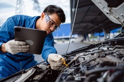 Automotive mechanic repairman using tablet and pulling dipstick to checking engine oil level engine in the engine room, check the mileage of the car, oil change, auto maintenance service concept.