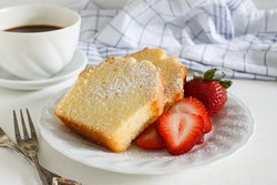 Sliced delicious pound cake with fresh strawberries and icing sugar for breakfast served with hot espresso in white cup.