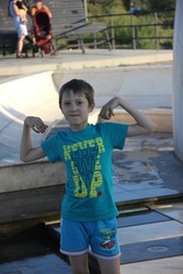 A beautiful child boy walks in the park, smiles, near the fountain, sculptures and carousels in the summer