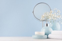 Delicate elegant ceramic decorations for bathroom - soft blue bowls, vase, white flowers, towel and soap on white wood table. Modern bath interior.
