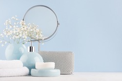 Dressing table with circle mirror, cosmetic silver accessories and white small flowers in ceramic pastel blue vase on white wood board.
