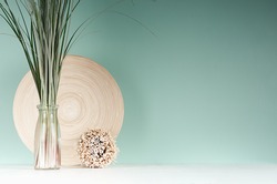 Natural light accessories for home decor - bamboo plate, bouquet of reed in glass bottle, decorative round sheaf of twigs in green mint menthe interior, white wood table.