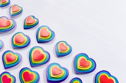 Bright rainbow hearts on white wood board, pattern, border, top view.