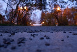 Small gravel stones on the paved path in a park with blurred background. Autumn sunset view.