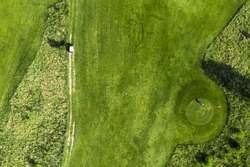 Top view of a green golf field with beautifully cut grass and trees.